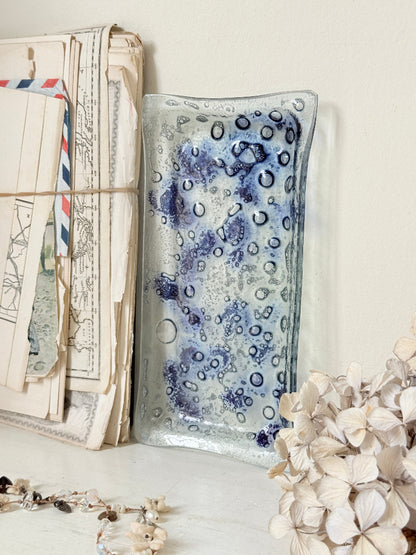 A rectangular glass tray with a blue and white spotted pattern, styled on a tabletop next to vintage letters and dried flowers.
