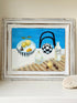 Still life oil painting showing fruit bowl and striped jug on a blue background, framed in white wood, photographed on a white surface.