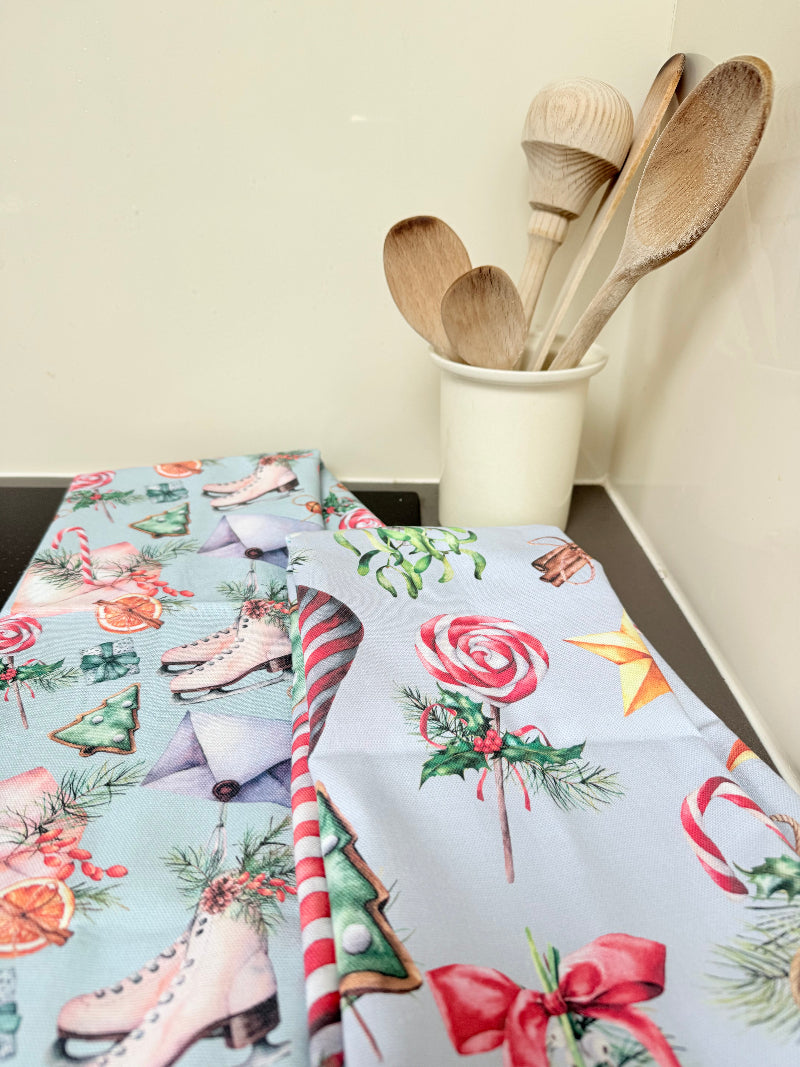 Pair of pastel blue festive tea towels with candy cane and ribbon print, folded, photographed on a kitchen worktop