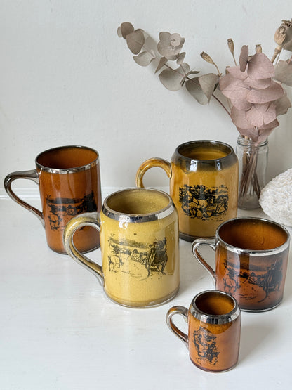 Set of 5 Ridgways stoneware mugs photographed on a white surface in amber brown glaze with black Coaching Days and Coaching Ways transfer scenes