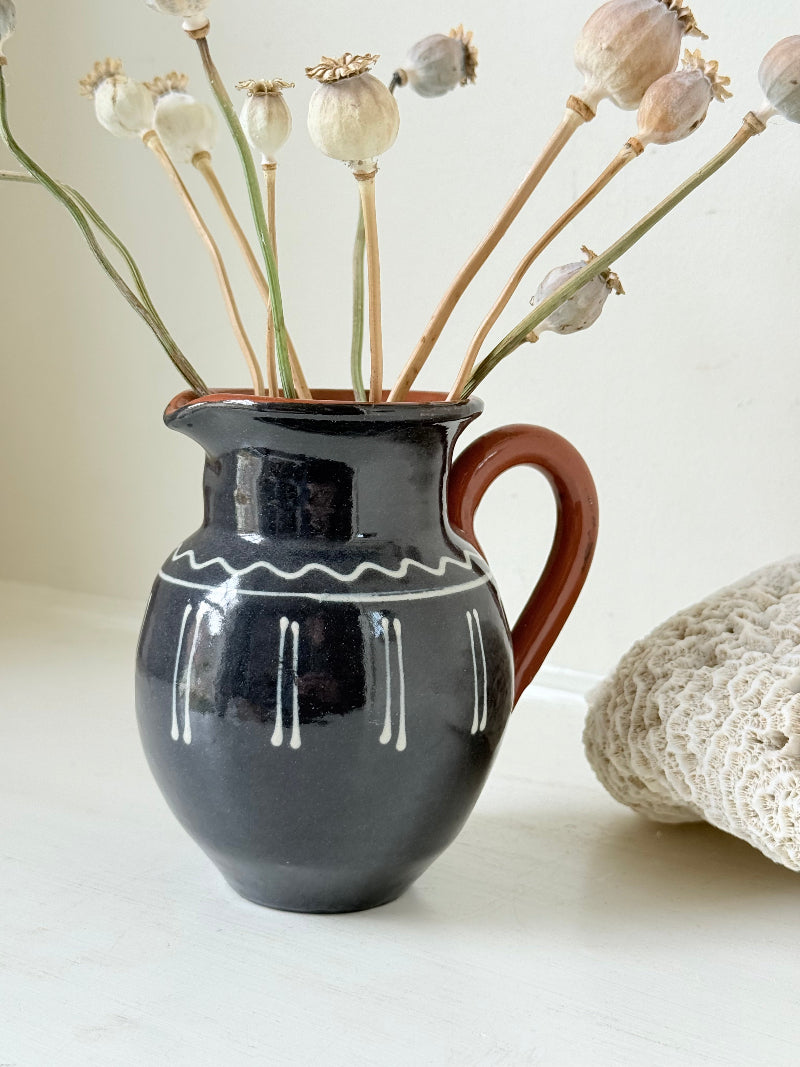 Slipware studio pottery jug with blue glaze and terracotta handle, photographed on a white surface