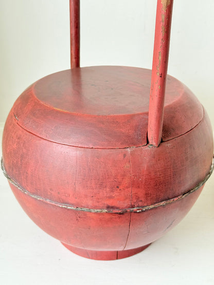 Vintage red painted wooden basket with tall curved handle and domed lid photographed on a white surface