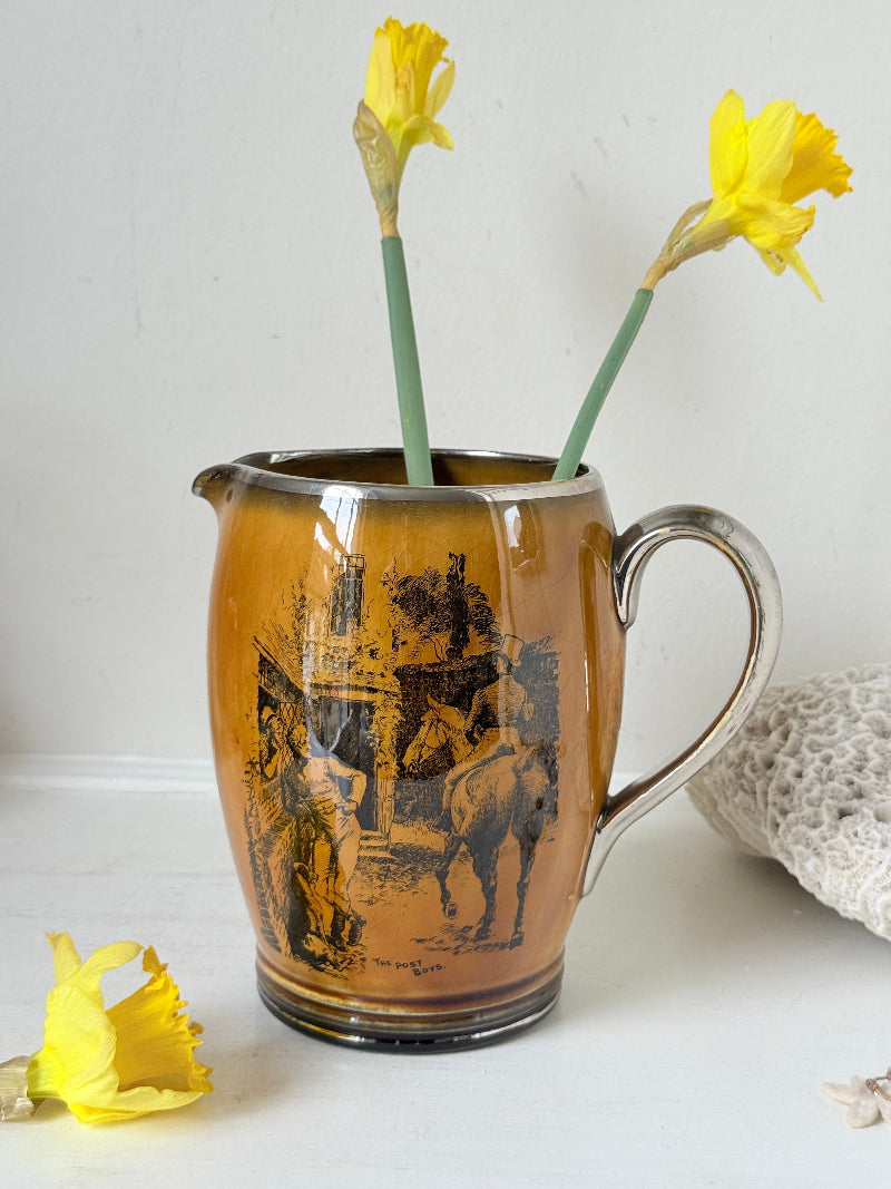 Antique Ridgways stoneware jug photographed on a white surface in amber treacle glaze with black Coaching Days and Coaching Ways transfer scenes and silver tone handle