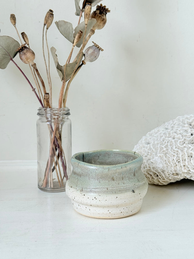 Studio pottery olive pot with soft green and cream glaze, photographed on a white surface