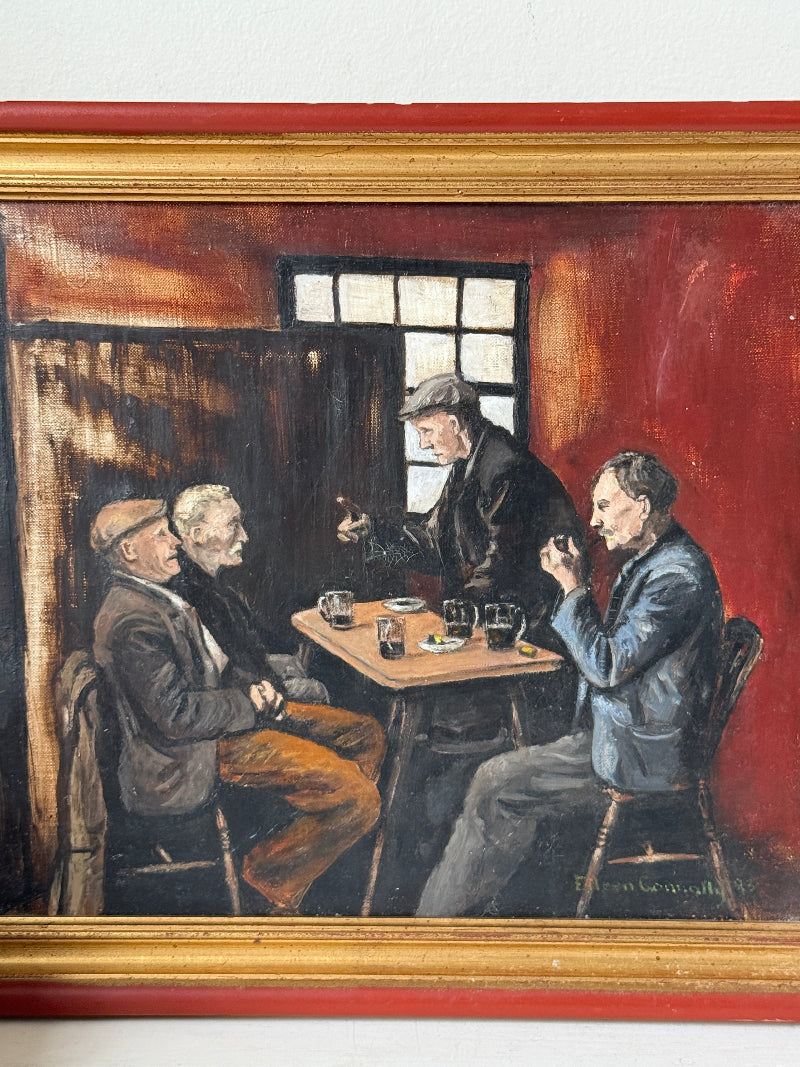 A framed oil painting depicting three men gathered around a small table in a dimly lit pub or cafe, with a red wall background and a gold-toned frame.