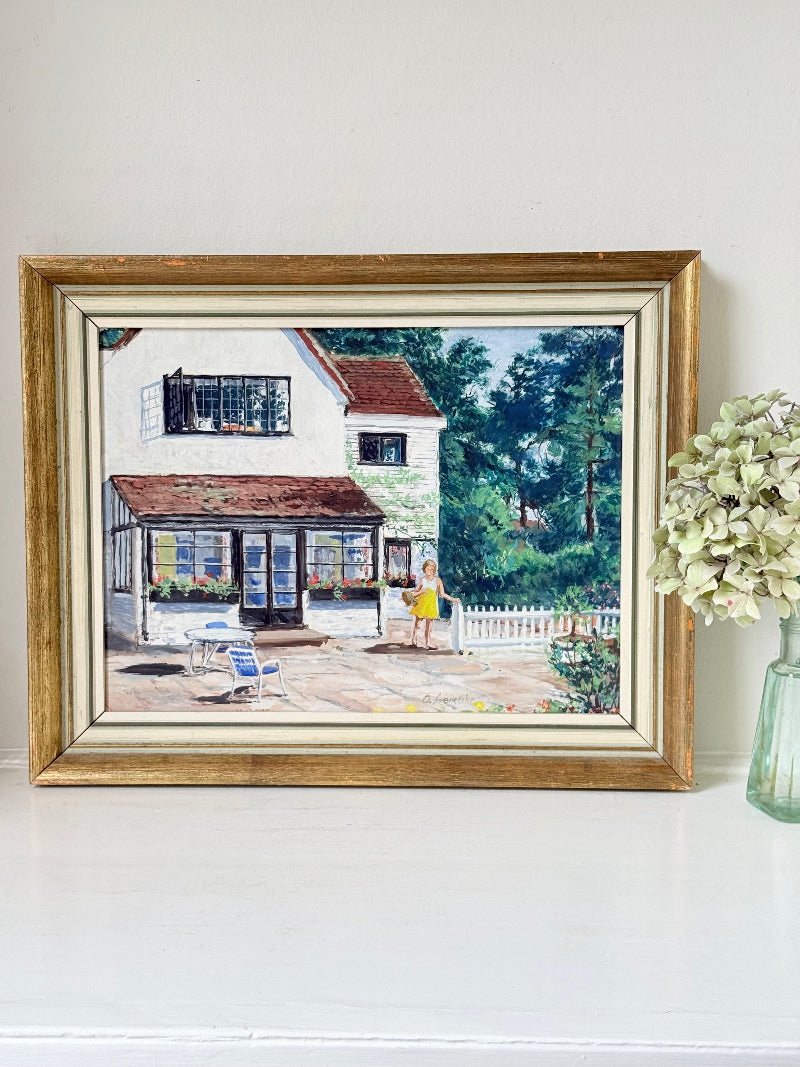 Oil on board painting of a girl in a yellow dress outside a cottage with picket fence, framed, photographed on a white surface