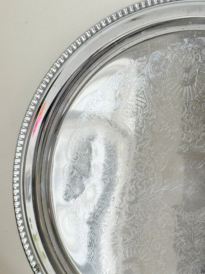 Vintage silver tone round tray with beaded edge, engraved surface detail and reflective finish for drinks or vanity styling