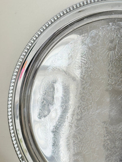 Vintage silver tone round tray with beaded edge, engraved surface detail and reflective finish for drinks or vanity styling