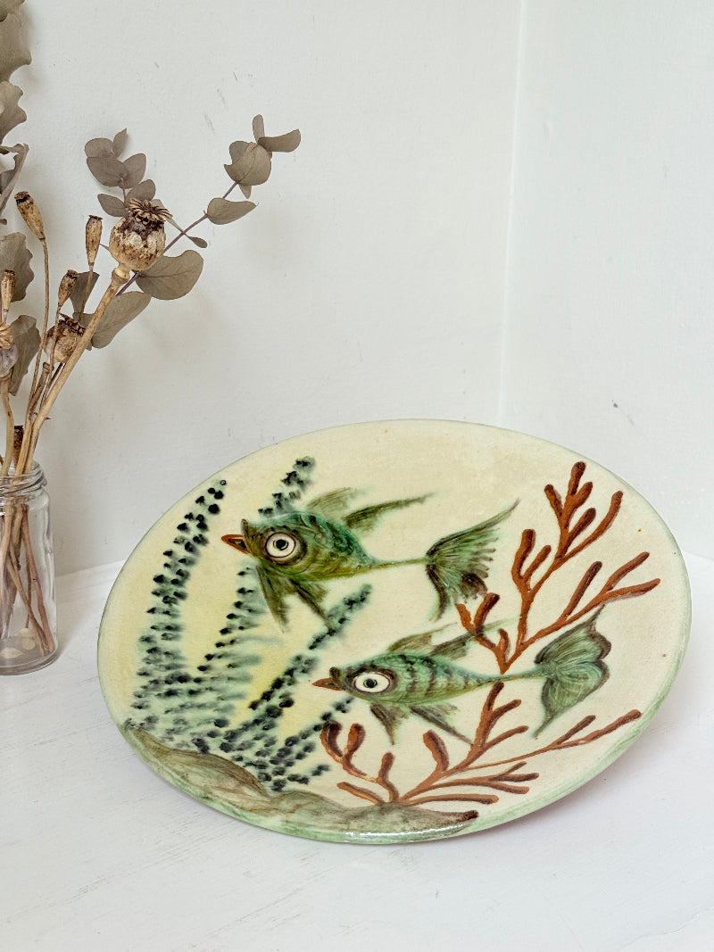 Puidgemont Spanish studio pottery plate with hand painted fish and coral design in green, turquoise, and terracotta tones, photographed on a white surface.