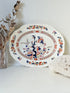 Vintage oval serving platter with chinoiserie style blue and red pattern photographed on a white surface
