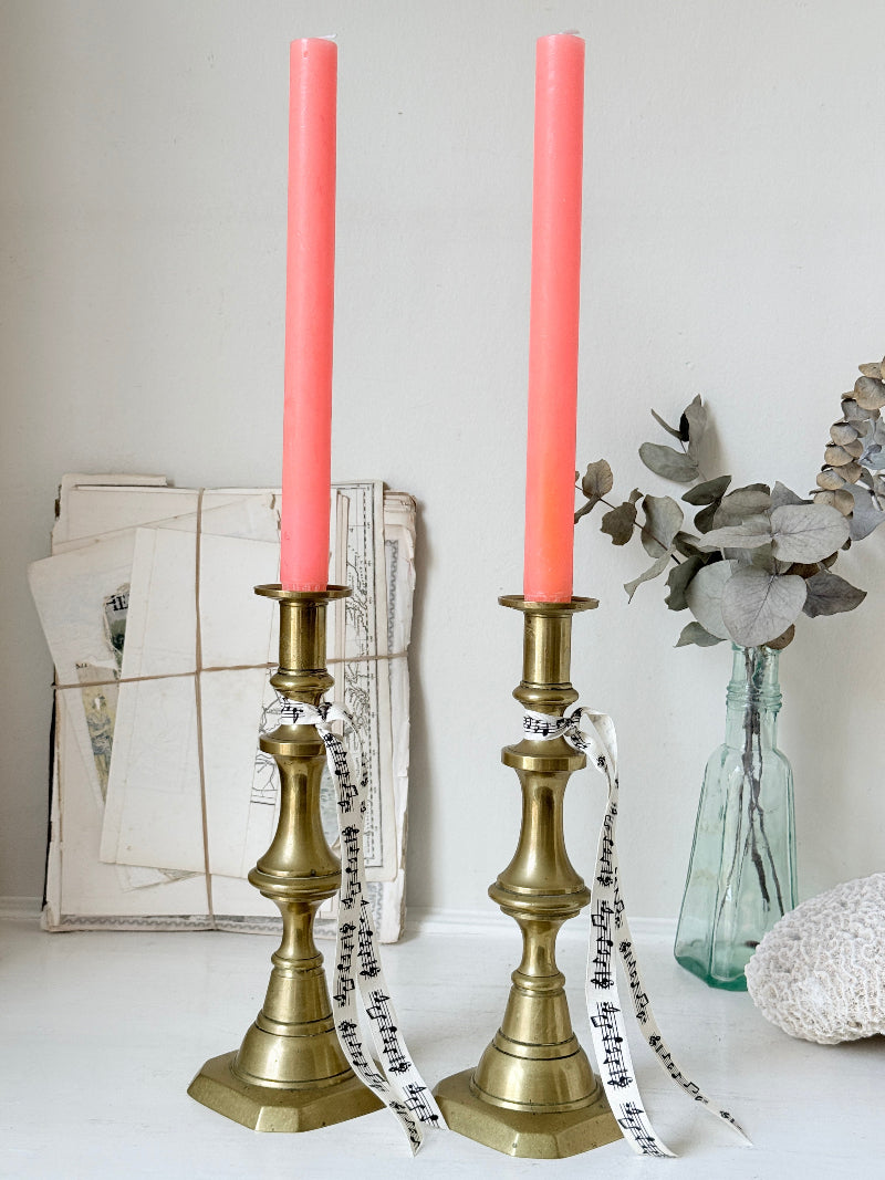 Pair of antique brass candlesticks with turned baluster stems and stepped bases holding coral tapers