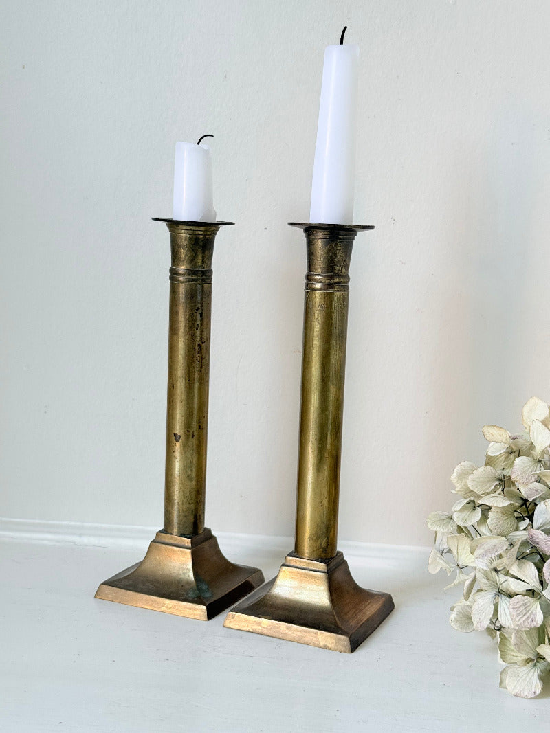 Pair of vintage brass candlesticks with square bases and white taper candles, styled on a white surface beside dried hydrangeas.