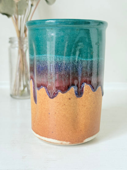 Studio pottery pen pot with teal and plum drip glaze, photographed on a white surface