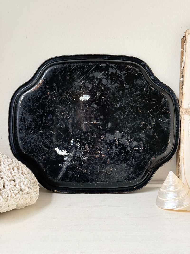 A distressed black ceramic serving tray with scalloped edges, resting on a white surface next to decorative seashells.