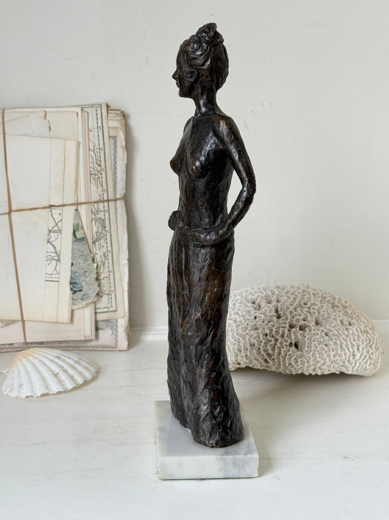 Solid bronze figure of a standing semi nude woman with upswept hair on a white marble base