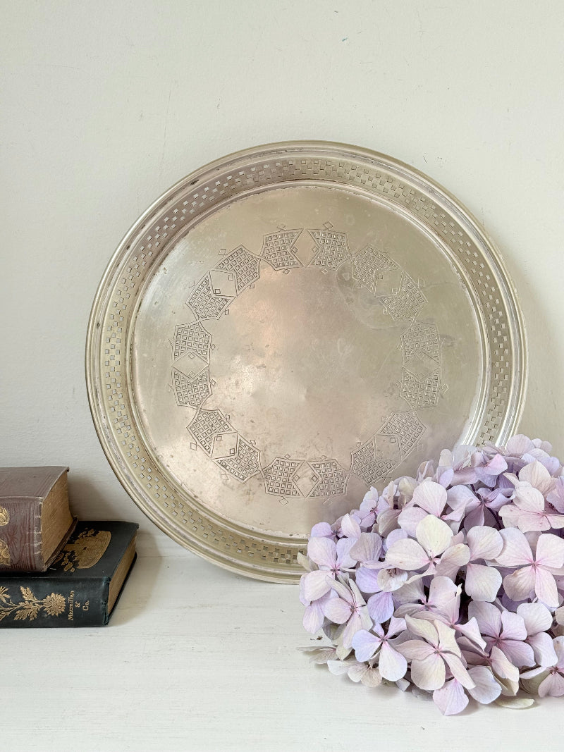 Vintage round silver plate tray with brass rim, pierced edge and etched central motif, photographed on white surface