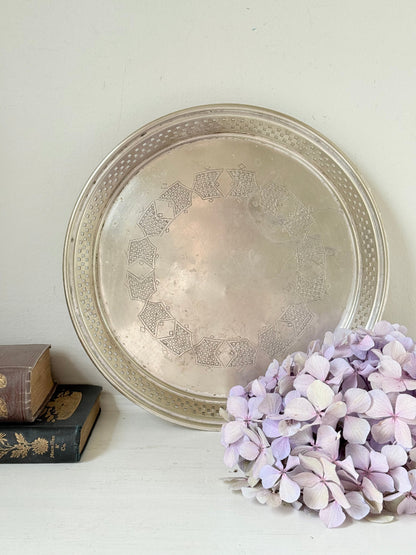 Vintage round silver plate tray with brass rim, pierced edge and etched central motif, photographed on white surface