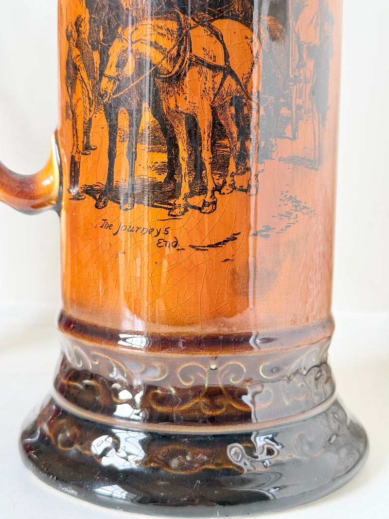Antique Ridgways stoneware jug photographed on a white surface in amber treacle glaze with A Christmas Visitor black transfer scene and tall handle