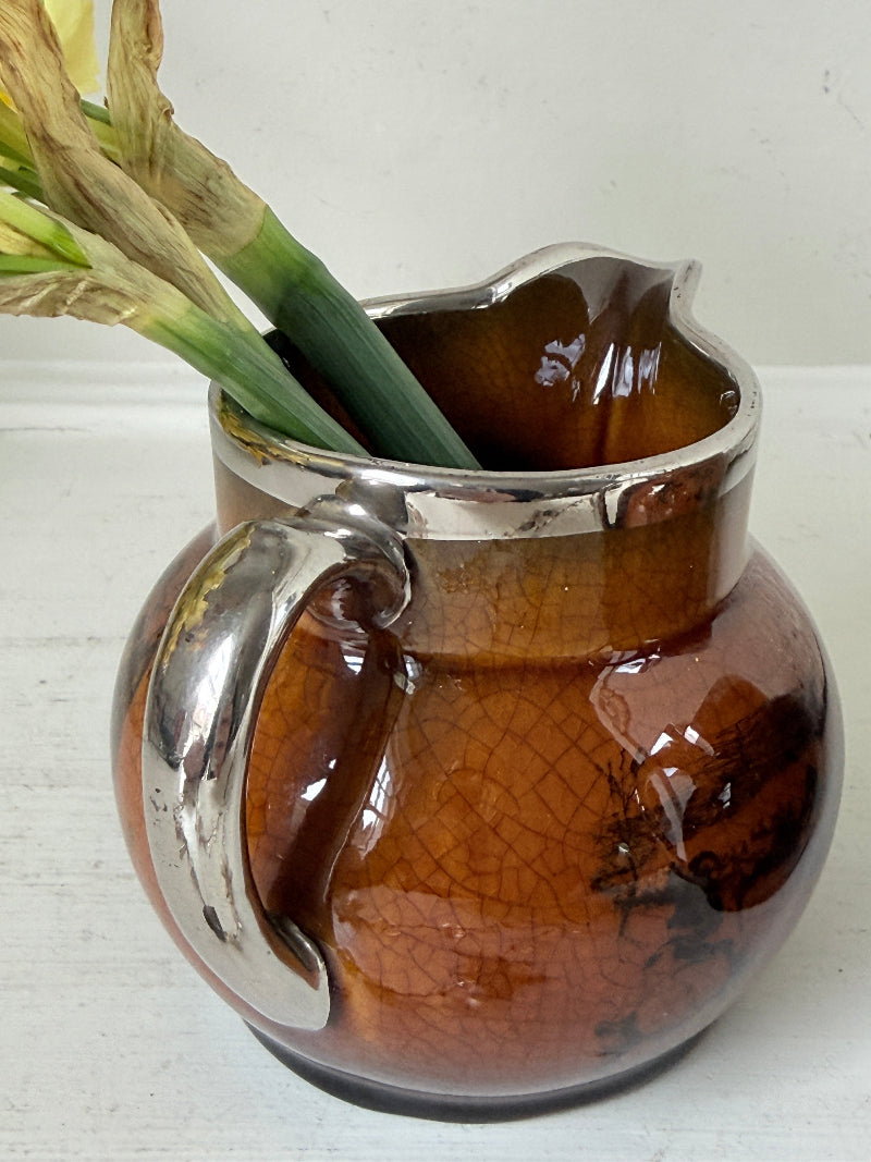 Pair of antique Ridgways stoneware creamer jugs photographed on a white surface in amber treacle glaze with black coaching scenes and silver lustre rims