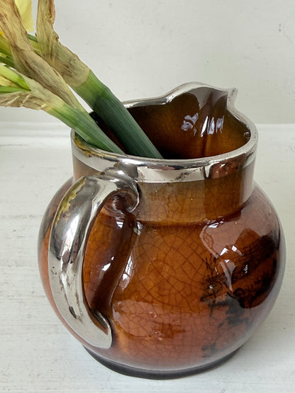 Pair of antique Ridgways stoneware creamer jugs photographed on a white surface in amber treacle glaze with black coaching scenes and silver lustre rims