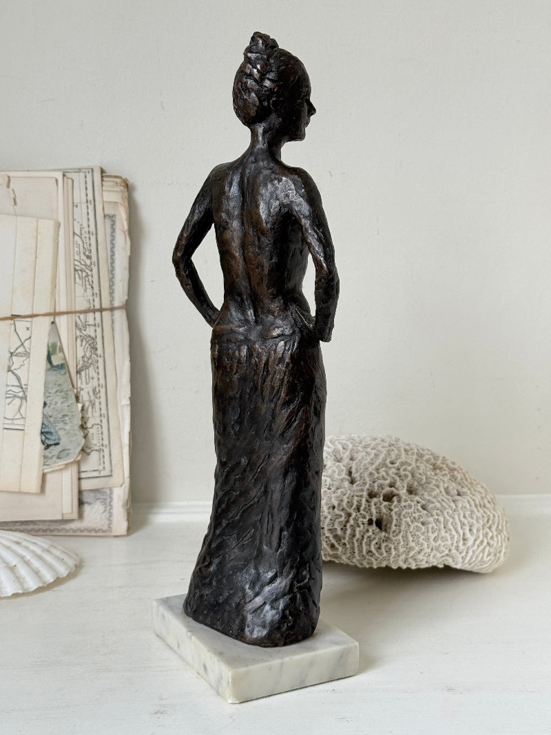 Solid bronze figure of a standing semi nude woman with upswept hair on a white marble base