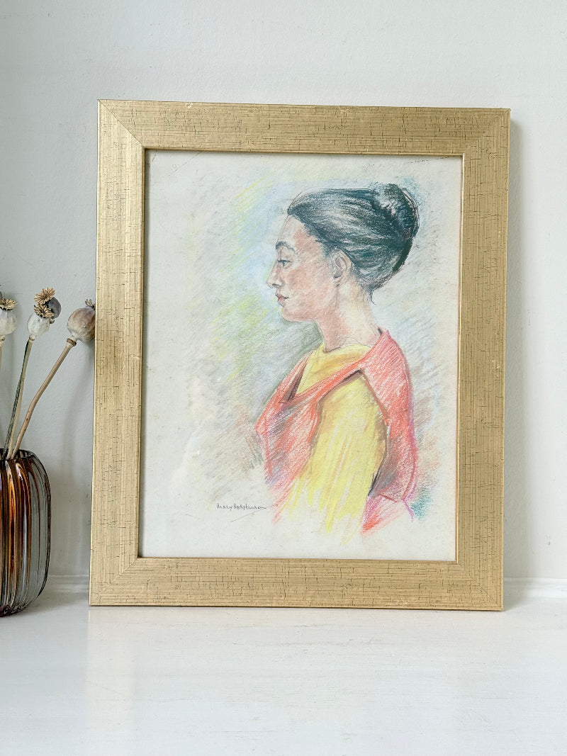 Vintage pastel portrait of a woman in profile wearing red and yellow, framed under glass, photographed on a white surface