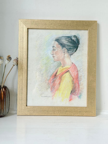 Vintage pastel portrait of a woman in profile wearing red and yellow, framed under glass, photographed on a white surface