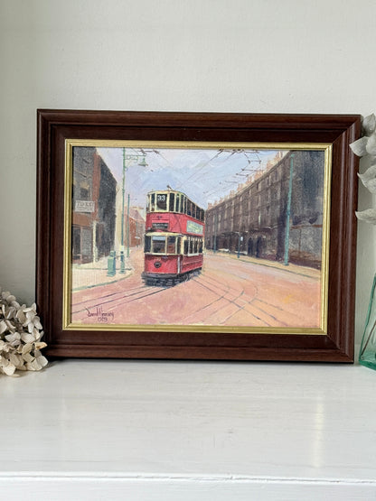 A framed vintage oil painting of a red double-decker tram on a city street, set in a dark brown wooden frame with a gold inner border, resting on a white surface.