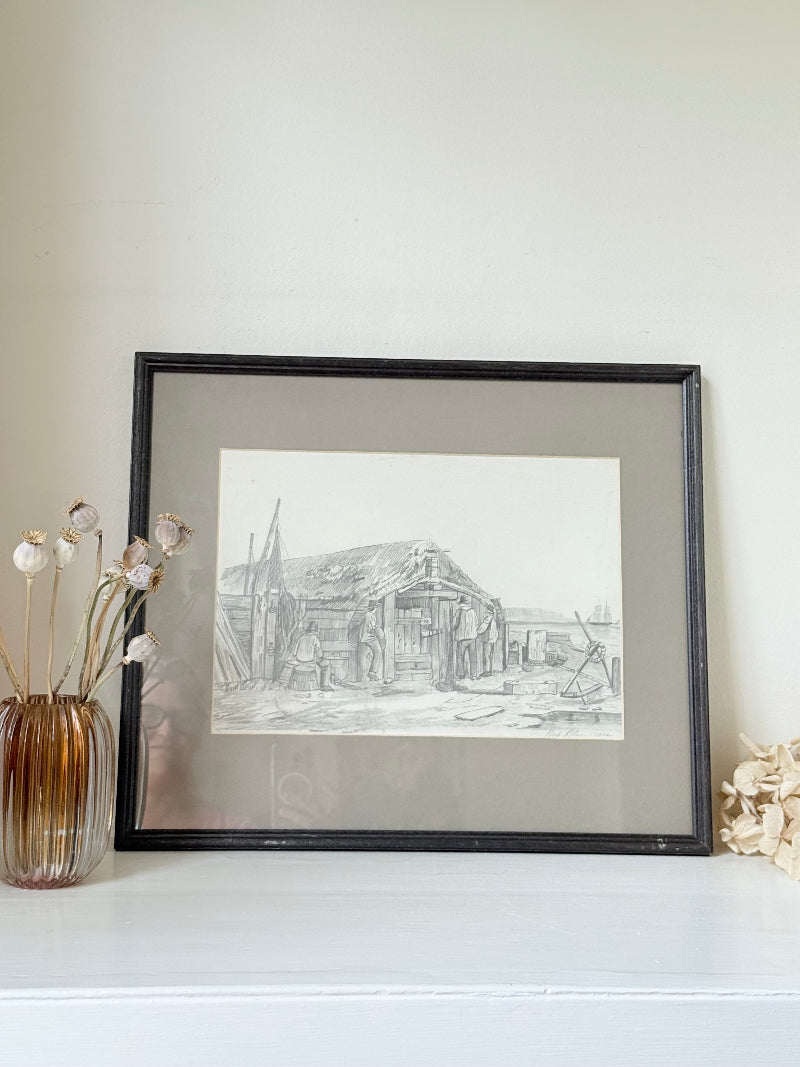 Vintage pencil drawing of rural scene with outbuildings and figures, under glass in black wooden frame, photographed on white surface.