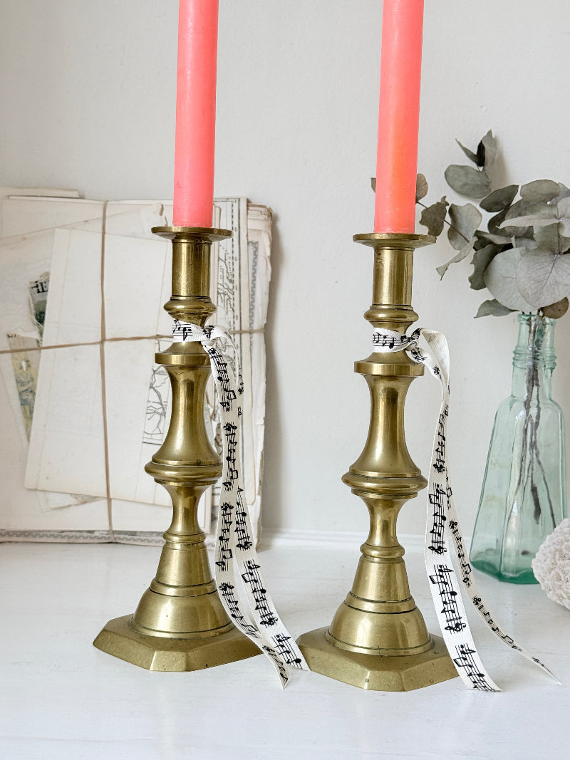 Pair of antique brass candlesticks with turned baluster stems and stepped bases holding coral tapers