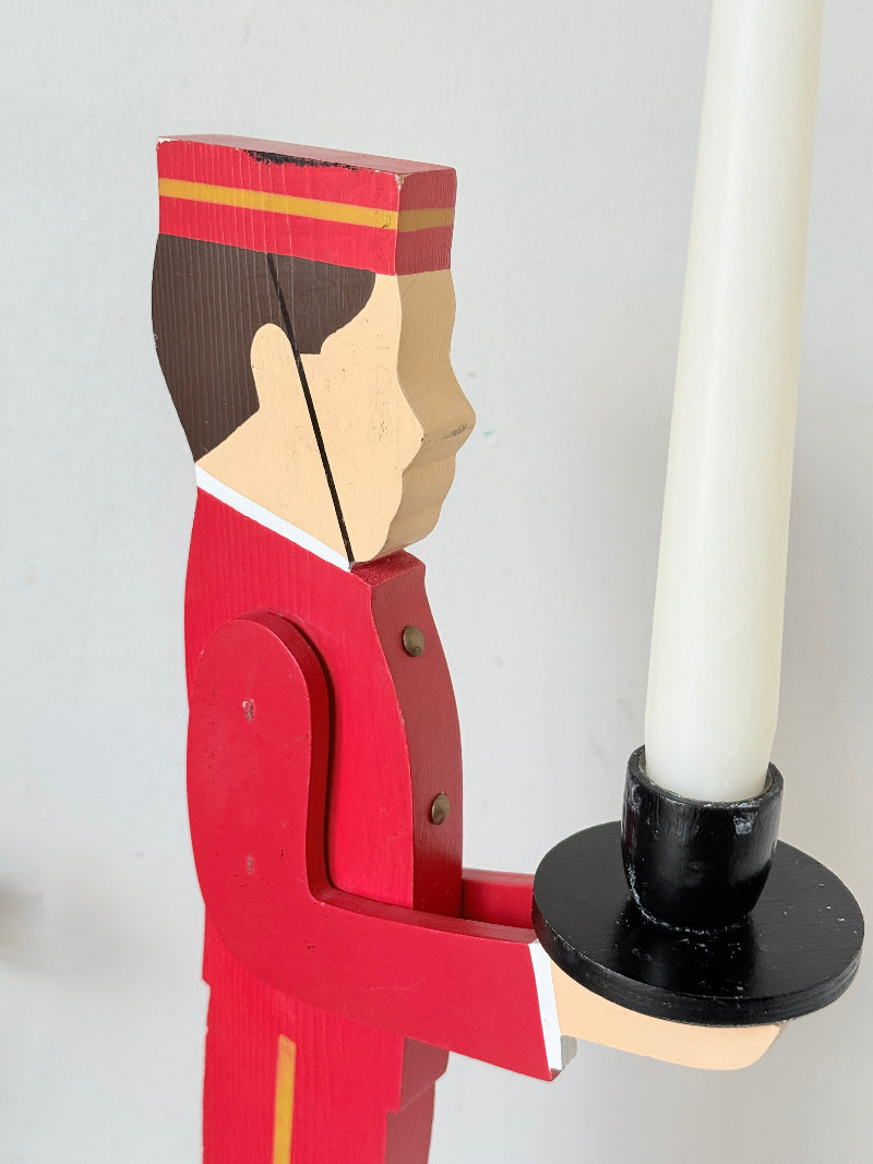 Vintage bellboy candlestick holder in red and black holding a tray with candle, photographed on a white surface