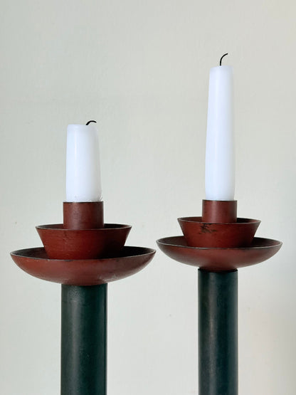 Pair of tall vintage metal candlesticks in black and burgundy, styled with white taper candles on a white surface.
