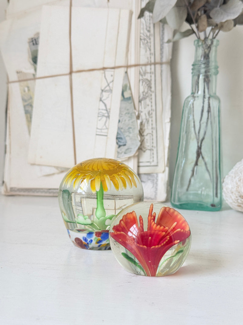 Pair of yellow and red flower glass paperweights with green stems, photographed on a white surface