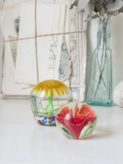 Pair of yellow and red flower glass paperweights with green stems, photographed on a white surface