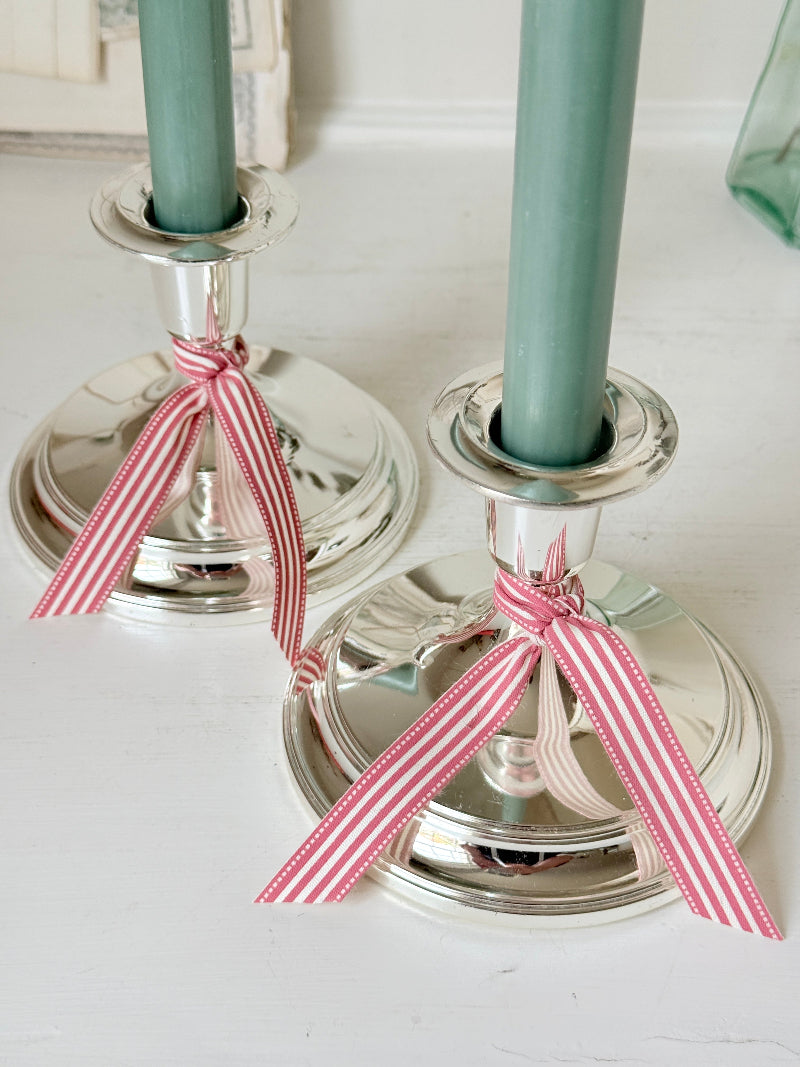Pair of silver tone candlesticks with wide round stepped bases holding green candles, photographed on a white surface
