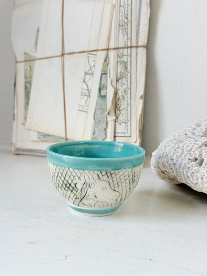 Hand thrown studio pottery bowl with turquoise glaze and hand decorated giraffe photographed on a white surface