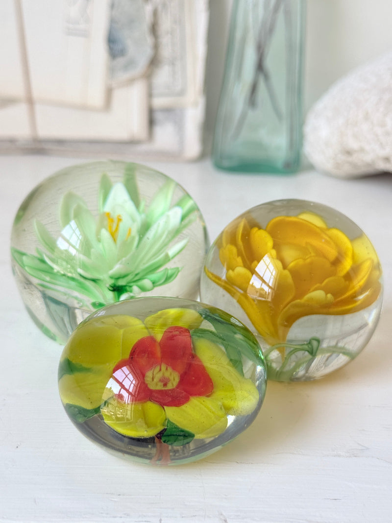 Trio of mixed flower glass paperweights in green, yellow and red, graduated in size, photographed on a white surface