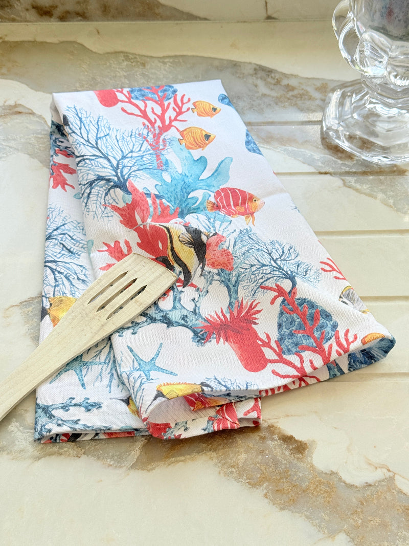 Coral reef print cotton tea towel in crisp white with colourful coral and tropical fish motifs, photographed indoors