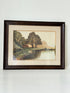 Antique framed rural watercolour of river, trees, and red-roofed building, in dark wooden frame with cream mount, on white surface.