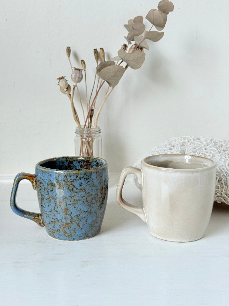 Pair of Christmas mugs with Santa and snowman designs photographed on a white surface.