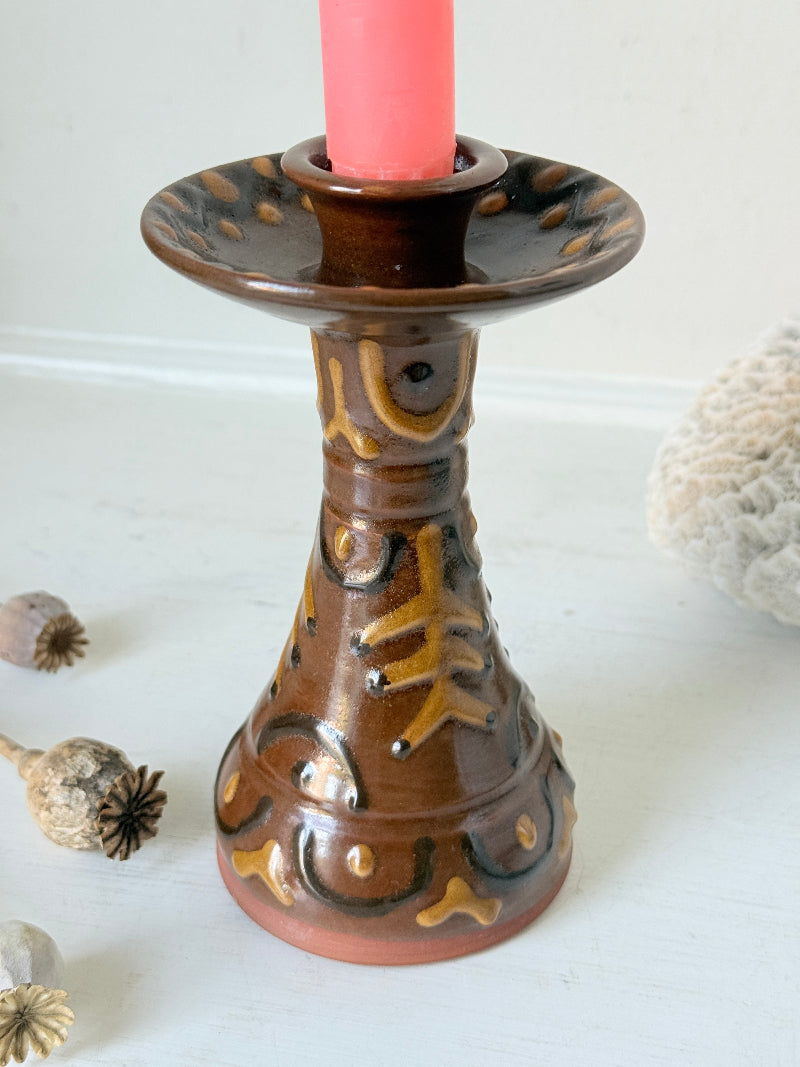 Vintage studio pottery candlestick in brown glaze with cut out decoration styled with coral taper candle on white surface