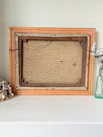 An antique wooden picture frame, shown from the back, resting on a white surface against a light beige wall. The frame has a light orange-painted outer border, a darker brown inner frame, and a textured beige canvas backing.