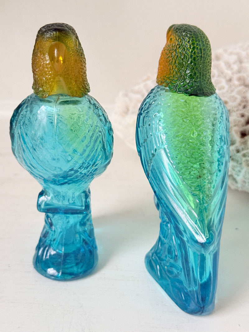 Pair of vintage Avon turquoise glass parrot bottles with green amber stoppers photographed on a white surface