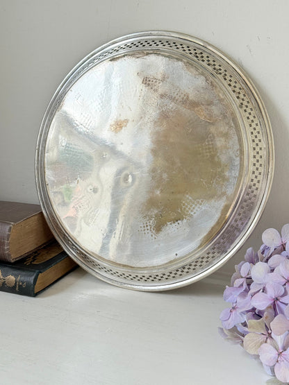 Vintage round silver plate tray with brass rim, pierced edge and etched central motif, photographed on white surface