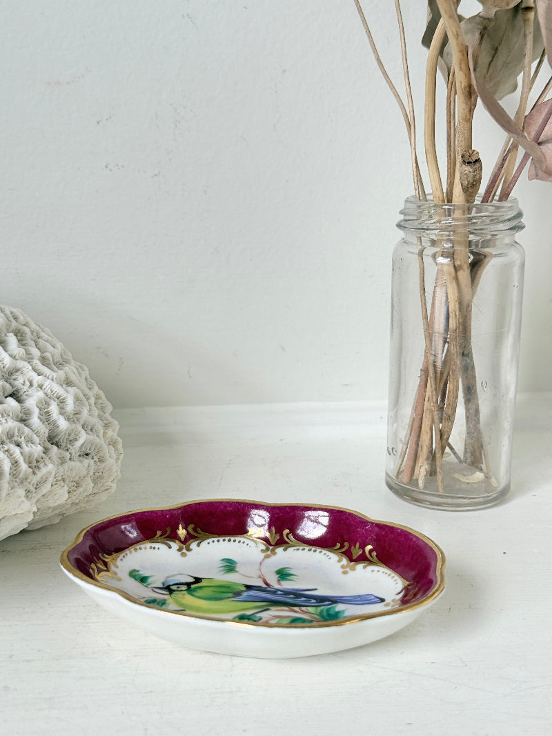 Vintage hand painted bird trinket dish with pink border and gilt detail photographed on a white surface