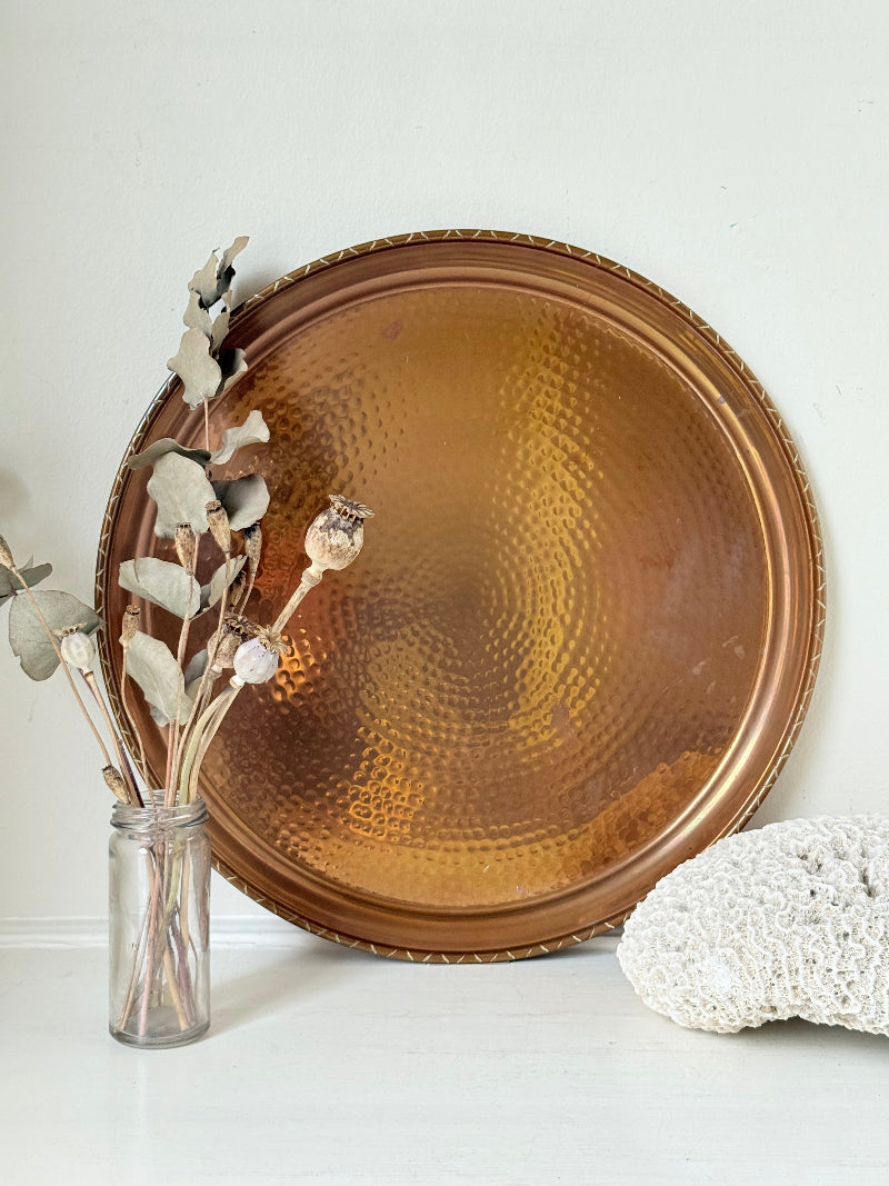 Lakeland Borrowdale hammered copper tray with warm patina, photographed on a white surface beside dried stems.