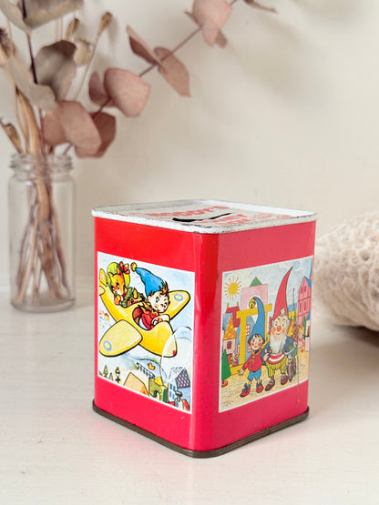 Vintage Noddy money box tin in red with illustrated panels, photographed on a white surface