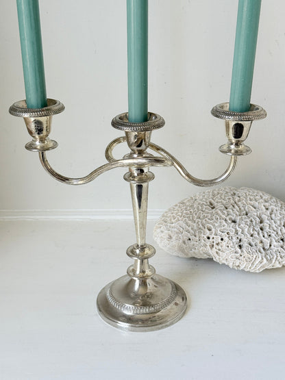Vintage silver plated three arm candelabra with gadrooned detail and blue green taper candles styled on a white surface
