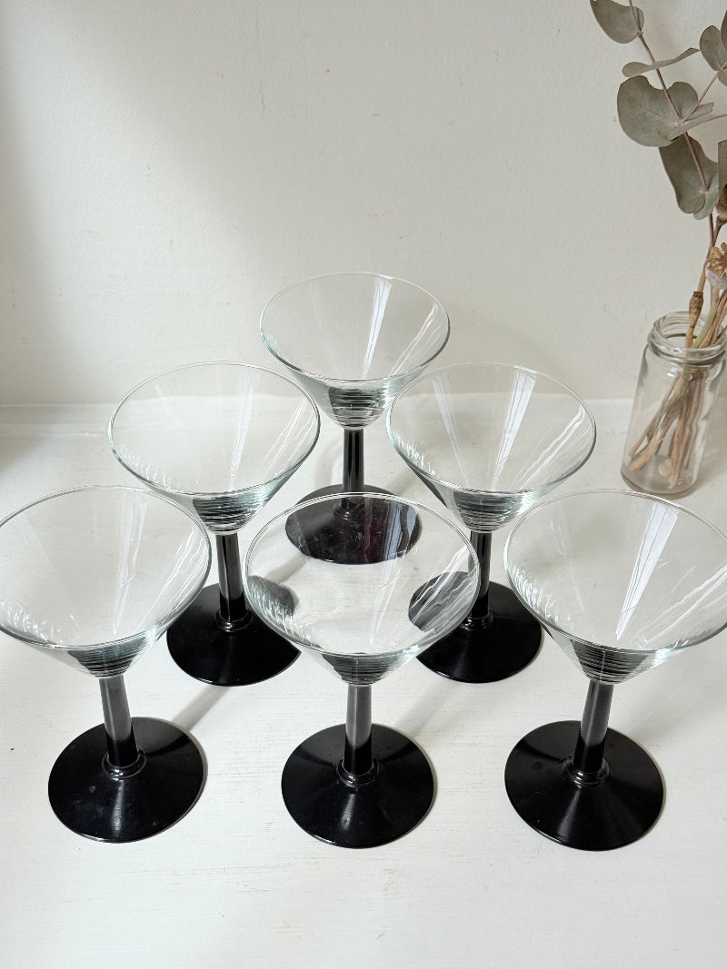 Set of six clear martini glasses with black stems, photographed on a white surface