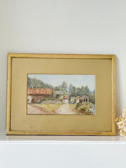 Framed vintage watercolour of countryside farm buildings with red roofs in gold frame photographed on a white surface